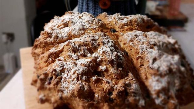 Freshly baked bread on a wooden board, with a hat visible in the background. Perfect for home baking enthusiasts!