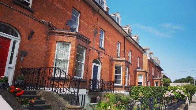 Red brick row houses with lush gardens and black wrought iron railings under a clear blue sky. Perfect for urban living.